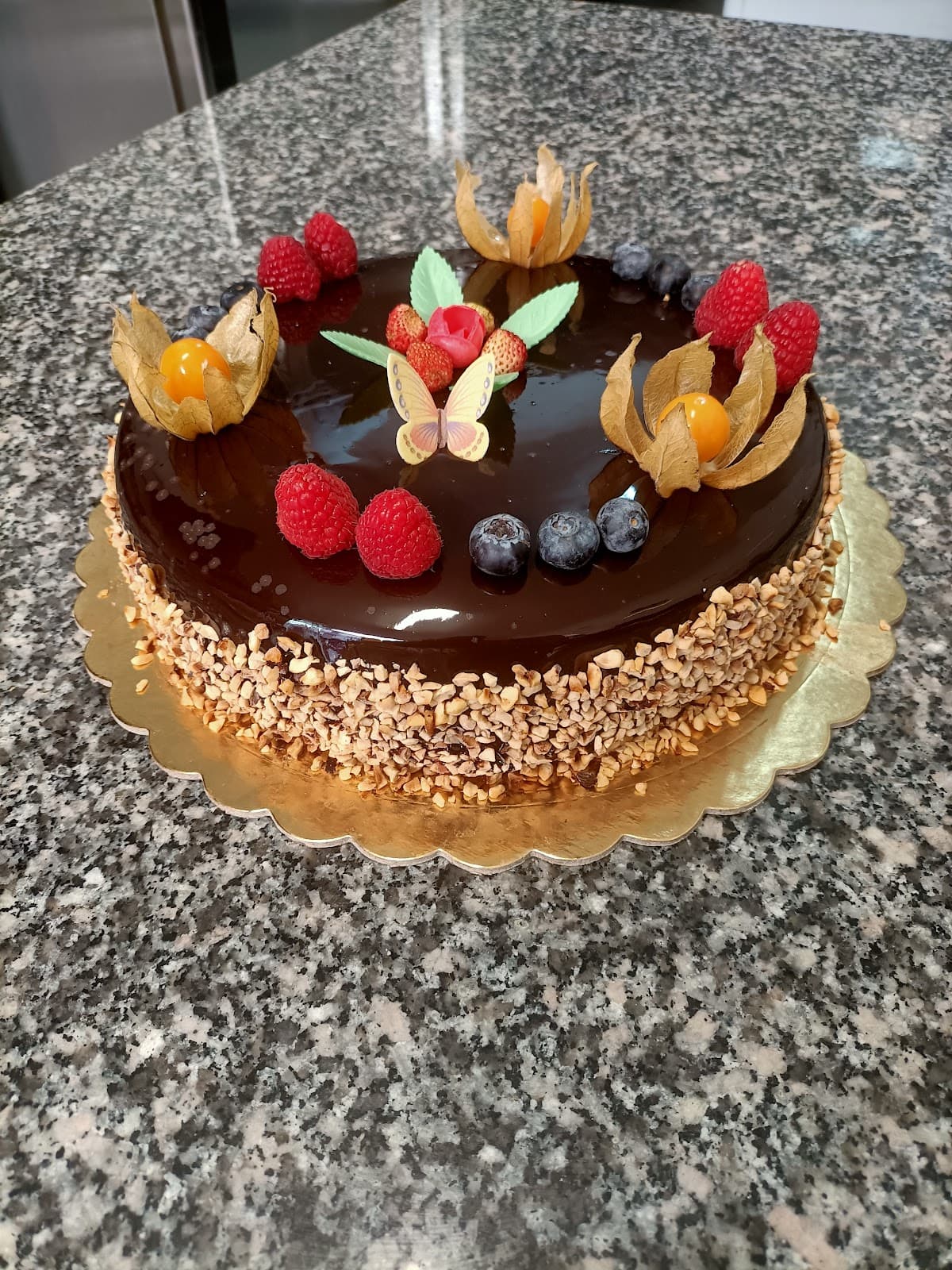 Torta al cioccolato decorata con lamponi, mirtilli, physalis e una farfalla di zucchero.