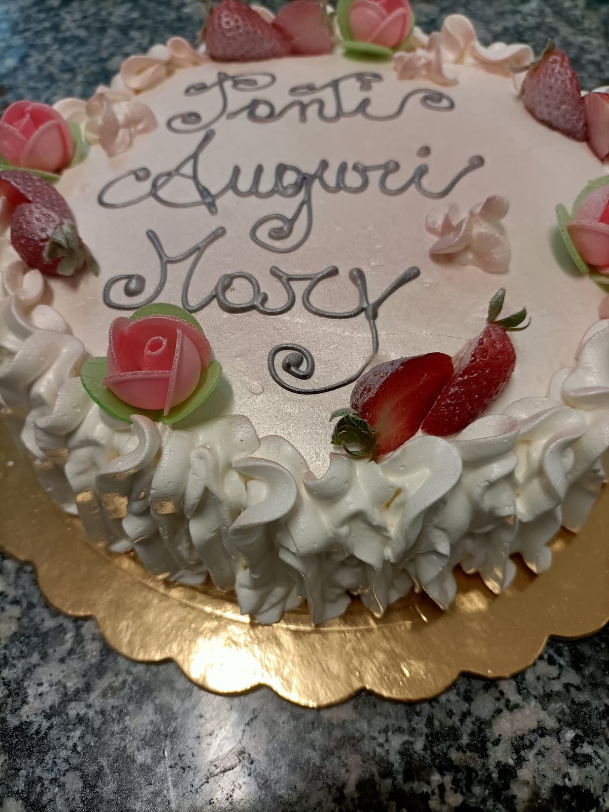 Torta di compleanno con panna, fragole e decorazioni floreali, con la scritta "Tanti Auguri Mary".
